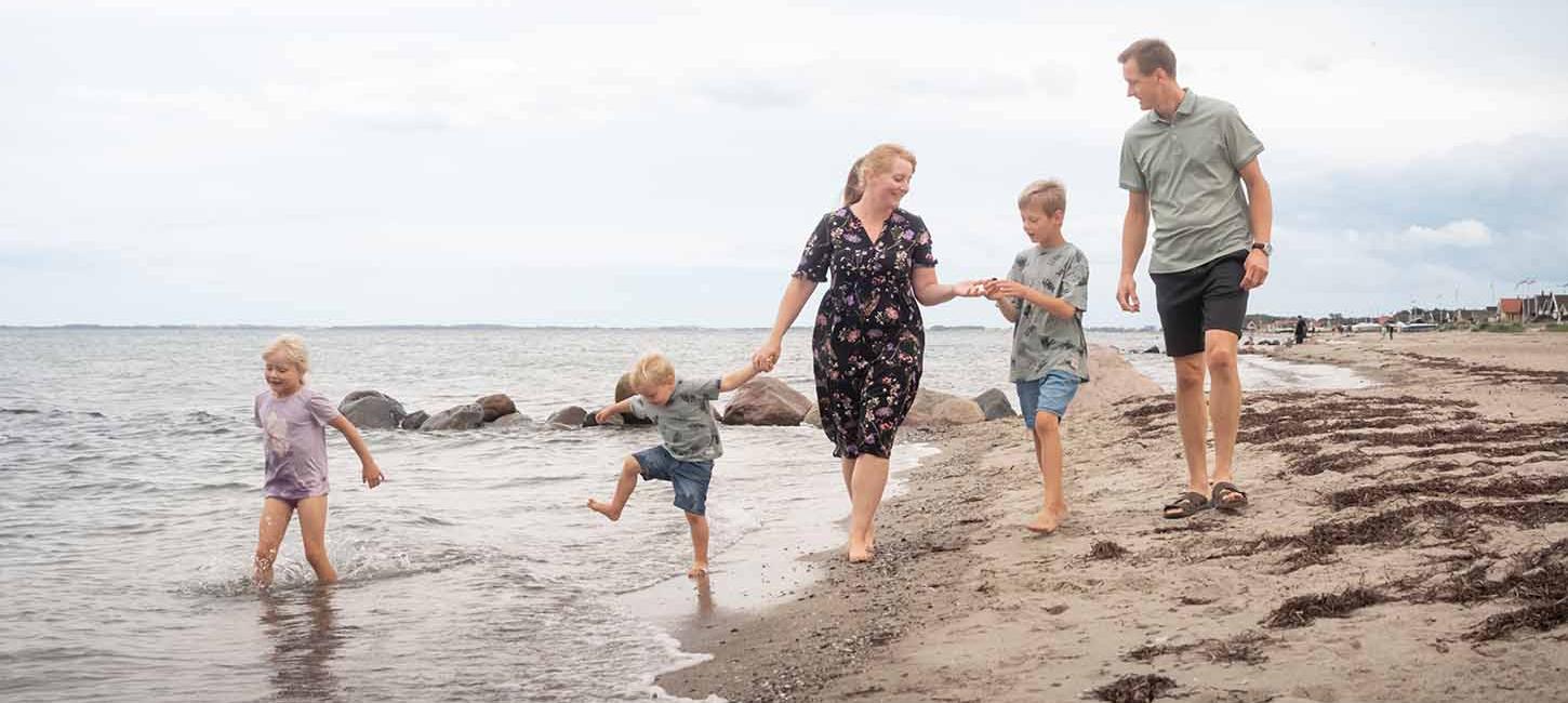 Familie går tur på Hasmark Strand og leger i vandet