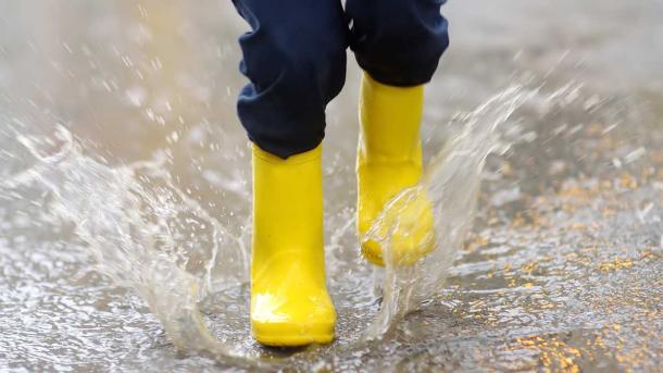 Et barn i gummistøvler hopper i regnvand