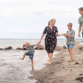 Familie går tur på Hasmark Strand og leger i vandet